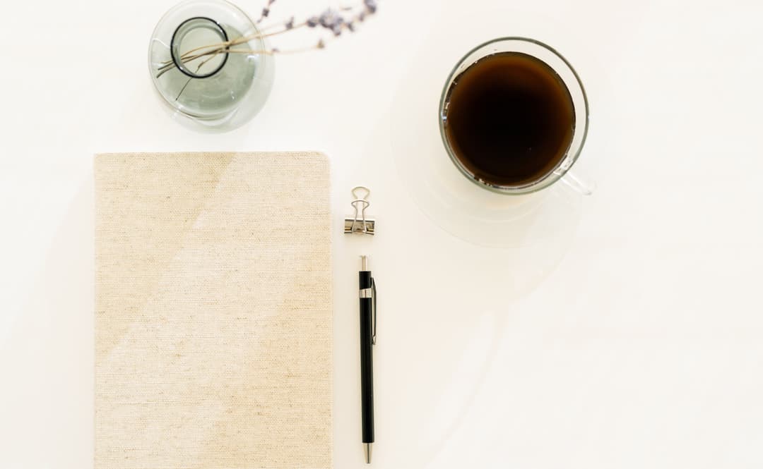 コーヒーと手帳とペンとガラスの小瓶に生けられた細身の花